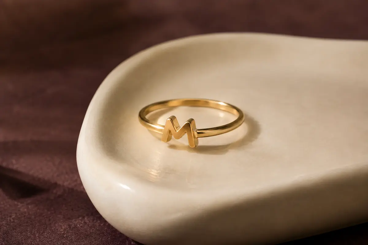 Bague minimaliste à motif de lettre présentée sur un support ivoire