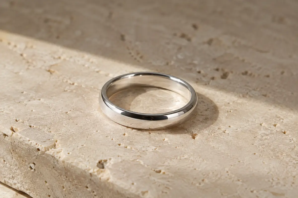 Alliance minimaliste en argent 925, anneau uni de 4 mm au poli brillant posé sur du travertin clair.