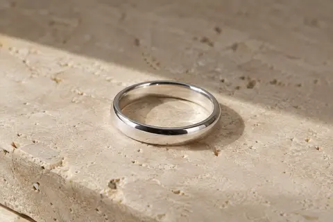 Alliance minimaliste en argent 925, anneau uni de 4 mm au poli brillant posé sur du travertin clair.