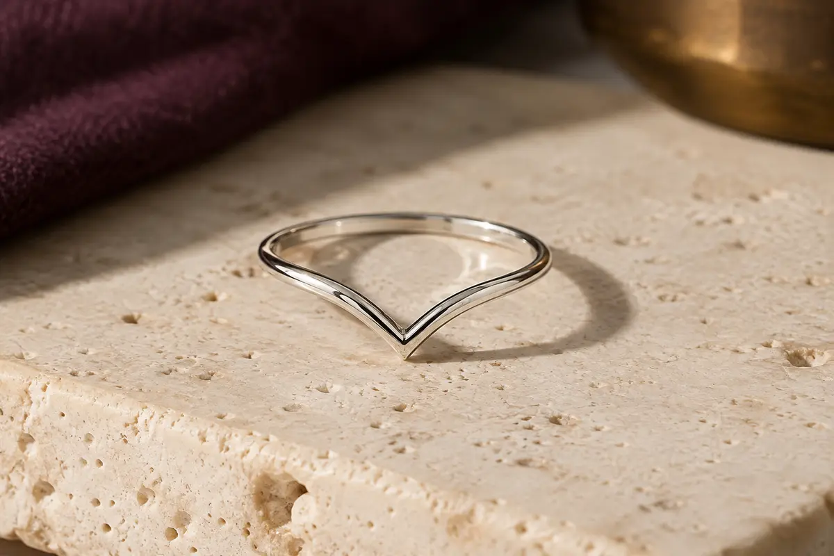 Bague fine en argent 925 à profil chevron, posée sur du travertin clair avec une finition polie brillante.