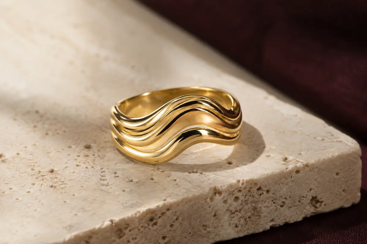 Bague Elli ondulée en argent 925 plaqué or, posée sur du travertin clair