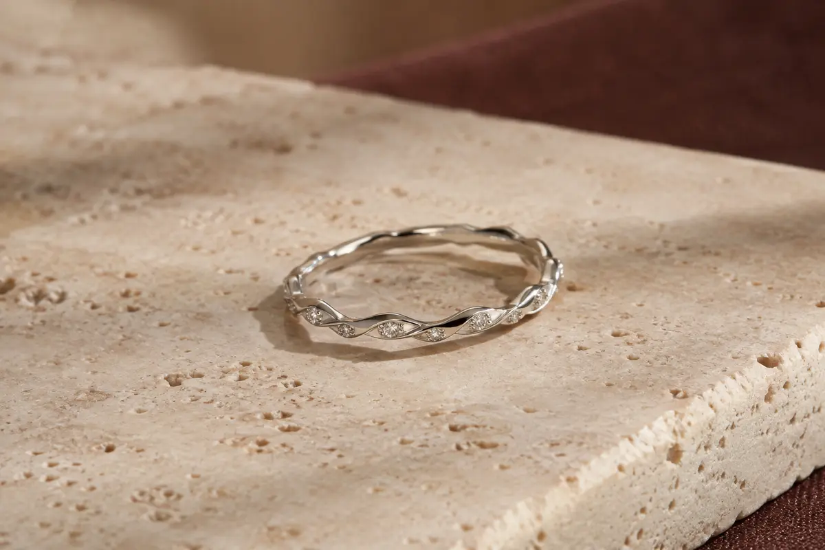Bague fine en argent 925/1000 à silhouette ondulée et oxydes de zirconium, posée sur du travertin clair.