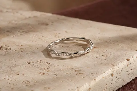 Bague fine en argent 925/1000 à silhouette ondulée et oxydes de zirconium, posée sur du travertin clair.