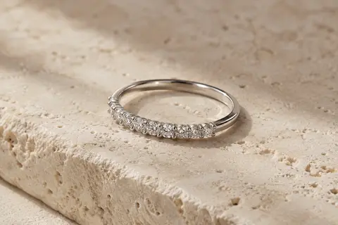 Bague fine en argent 925 rhodié, sertie de moissanites sur une demi-éternité et posée sur du travertin clair