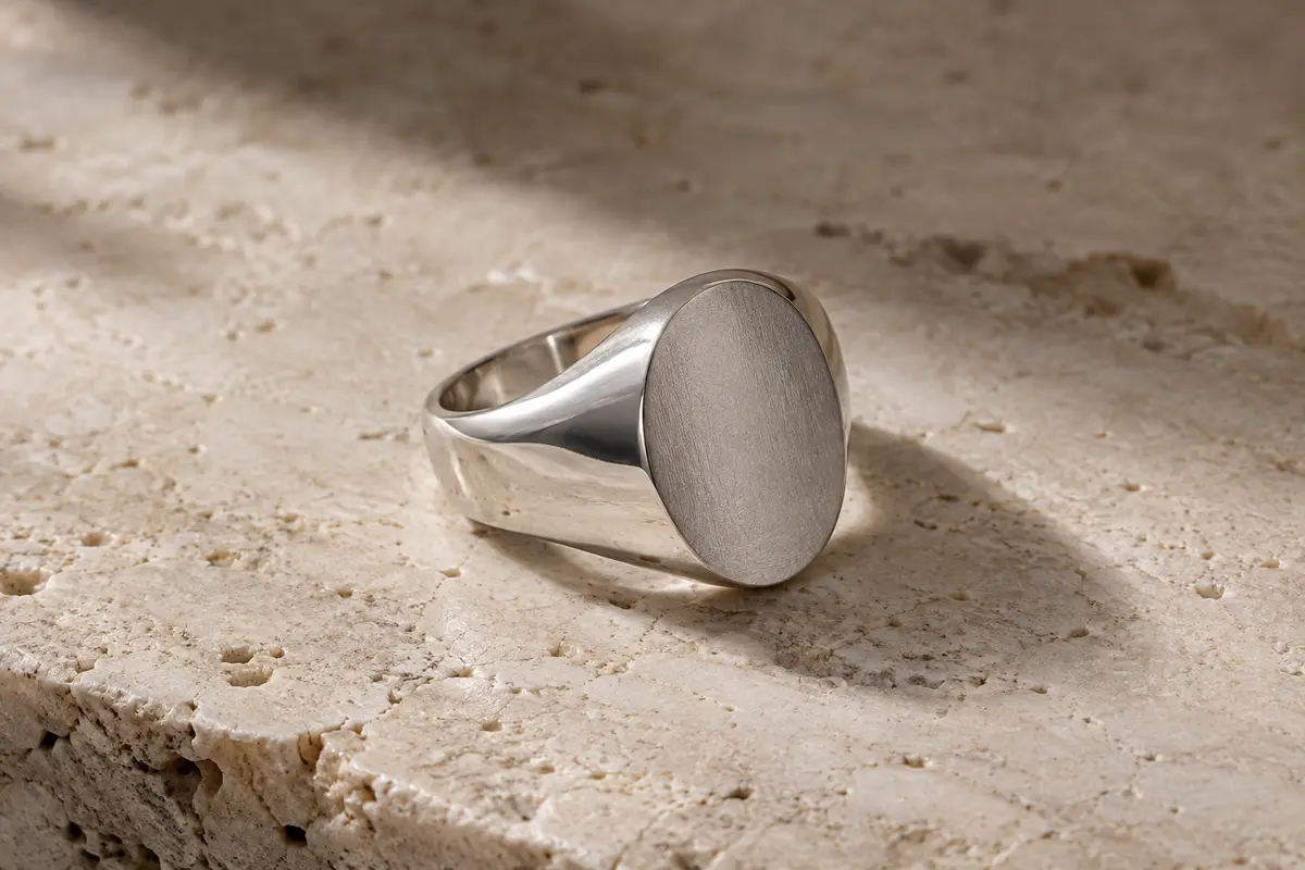 Chevalière ovale en argent 925 à surface mate, photographiée seule sur du travertin clair.