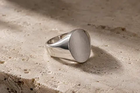 Chevalière ovale en argent 925 à surface mate, photographiée seule sur du travertin clair.