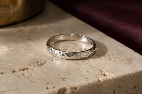 Bague fine en argent 925 à la surface martelée, posée sur du travertin clair sous une lumière douce.