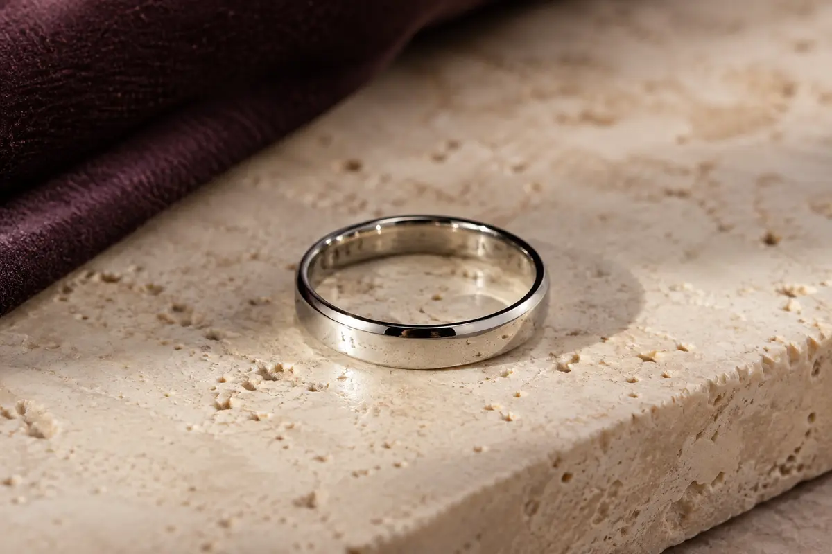 Bague unisexe argentée de 4 mm en acier inoxydable poli miroir, posée sur du travertin clair.