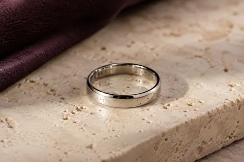 Bague unisexe argentée de 4 mm en acier inoxydable poli miroir, posée sur du travertin clair.
