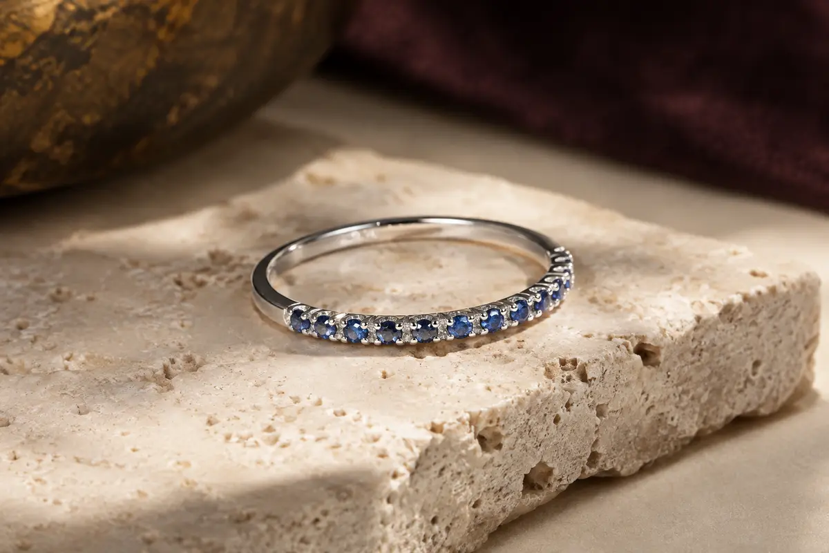Bague fine en argent 925 sertie de petits zircons bleus sur une demi-éternité, posée sur du travertin clair.