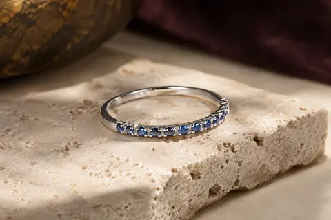 Bague fine en argent 925 sertie de petits zircons bleus sur une demi-éternité, posée sur du travertin clair.