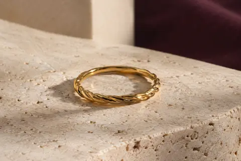 Bague fine dorée à surface torsadée posée sur du travertin clair, avec son relief délicat mis en lumière.