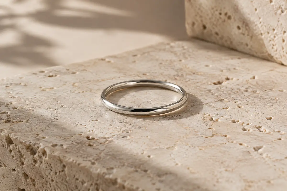 Bague fine en argent 925 à surface polie, posée sur une pierre de travertin clair.