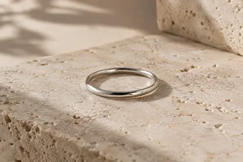 Bague fine en argent 925 à surface polie, posée sur une pierre de travertin clair.
