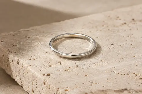 Bague fine argentée en acier inoxydable, posée sur du travertin clair avec sa surface brillante visible.