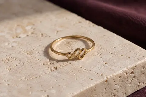 Bague fine à lettres en acier inoxydable à finition dorée, posée sur du travertin clair sous une lumière douce.