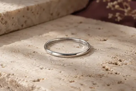 Alliance fine argentée de 2 mm posée sur du travertin clair, sous une lumière latérale douce.