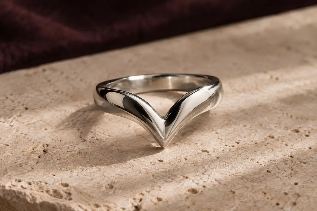 Bague chevron en argent poli posée sur du travertin clair, montrant sa silhouette sculptée en V.