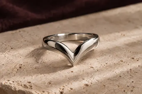 Bague chevron en argent poli posée sur du travertin clair, montrant sa silhouette sculptée en V.